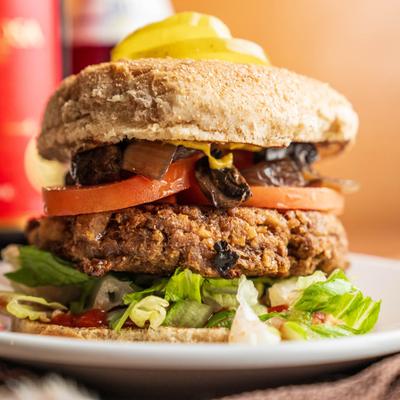 Veggie burger with lettuce, tomato, and mushrooms on a whole grain bun.